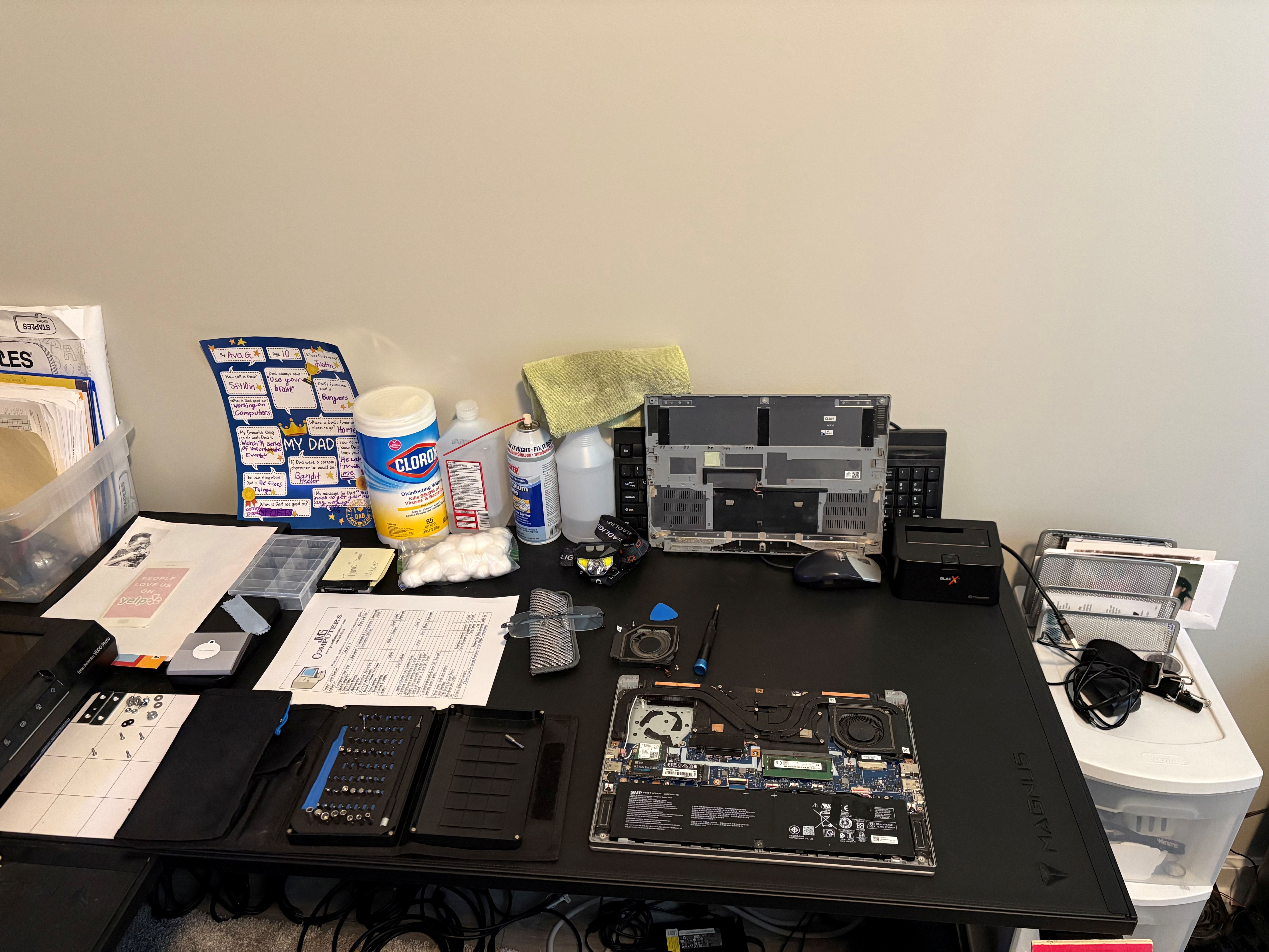 Close view of repair tools, parts, and an opened laptop on the workbench